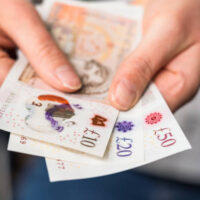 Close-up of a woman holding modern polymer ten, twenty and fifty pound notes.