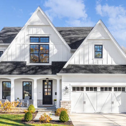 Oak Park, IL, USA - November 4, 2020: A new, white modern farmhouse with a dark shingled roof and black window frames. The bottom of the house has a light rock siding and covered front porch.