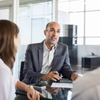 Mature financial agent showing new investment to young couple. Happy financial advisor discussing with a couple their mortgage loan. Happy couple consulting their bank agent about savings plan.